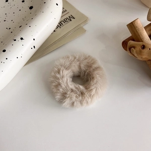 Dettaglio di un elastico per capelli in peluche beige chiaro su un tavolo bianco