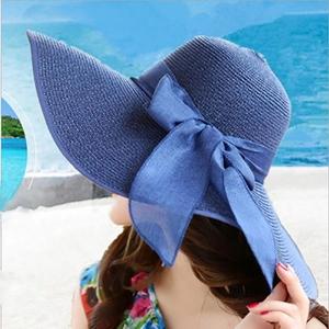 Women's blue straw sun hat with large bow on beach background for summer travel