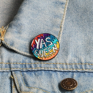 Detail of Yas Queen enamel pin on blue denim jacket showing colorful zigzag pattern