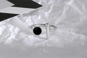 Macro detail of silver geometric ring with black enamel bead and bar on art background
