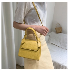 Detail of yellow crocodile pattern handbag with decorative knotted handle on sofa