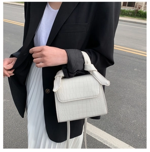 Street style shot of a white faux-crocodile pattern square bag with a knotted handle