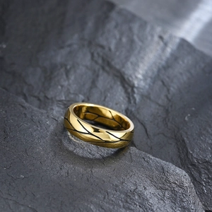 Minimalist gold metal ring with black vine leaf engraving on textured stone background