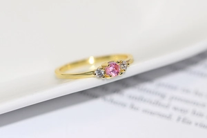 Macro shot of gold-plated three-stone ring with round pink gemstone and white cubic zirconia