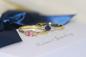 Macro view of gold plated three-stone rings with pink and blue round cut crystals