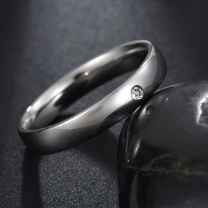 Polished stainless steel ring with a round zircon stone on a black pebble background