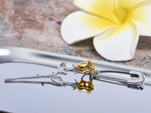 Macro shot of two-tone gold and silver rose safety pin earring on reflective tray