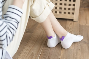 Detail of white low cut cotton socks featuring a purple 3D heart patch on the heel