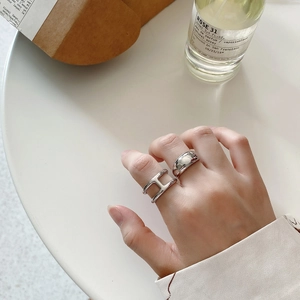 Close-up of a minimalist silver H-shaped ring and wide band worn on a hand