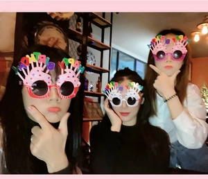 Three colorful cupcake-shaped Happy Birthday glasses with candles on a dark background
