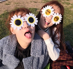 Detail view of two people wearing white daisy flower sunglasses on outdoor grass background