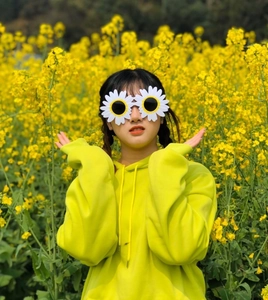 Outdoor shot of a person wearing daisy flower sunglasses and a yellow hoodie in a flower field