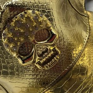 Détail du cuir doré gaufré crocodile avec tête de mort en strass et rivets métalliques
