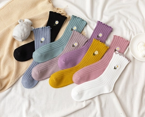 Detail of colorful rib-knit mid-calf socks with delicate lace edges and daisy embroidery