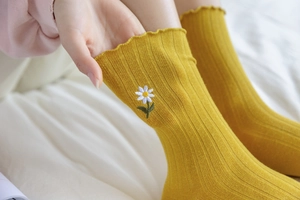 Close-up of yellow ribbed cotton sock featuring daisy embroidery and lettuce trim edge