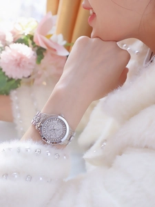 Close-up of luxury silver wristwatch with rhinestones on female wrist with flowers