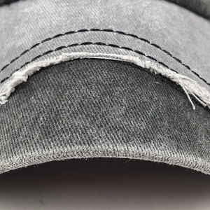 Detail of frayed edge design and black double stitching on dark gray baseball cap