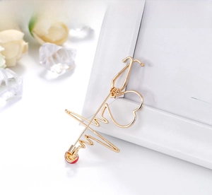 Detailed view of a gold medical stethoscope brooch with red heart and pulse line