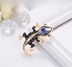 Macro shot of gecko brooch with black enamel, white crystals and a grey gemstone inlay