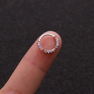 Makroaufnahme eines silbernen Nasenrings mit bunten Zirkoniasteinen auf einer Fingerspitze