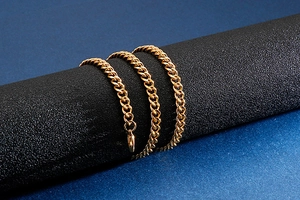 Detailed view of a golden curb chain necklace wrapped around a black matte prop