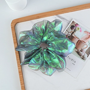 Macro shot of an iridescent pleated scrunchie with metallic sheen on marble tray