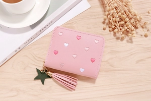 Pink PU leather wallet with heart embroidery, tassel, and star charm on wood background