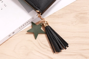 Detail of black faux leather wallet with golden zipper, tassel, and star charm