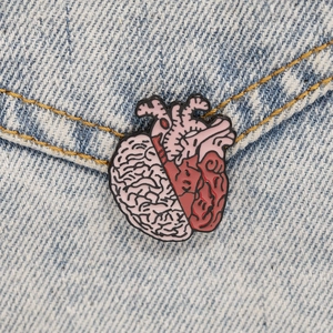 Detail of anatomical heart and brain enamel pin on blue denim fabric background