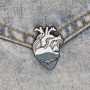 Macro view of anatomical heart enamel pin with whale and wave design on denim jacket