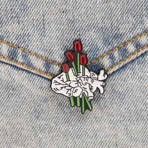Detailed close-up of a hand holding red tulips brooch on blue denim fabric