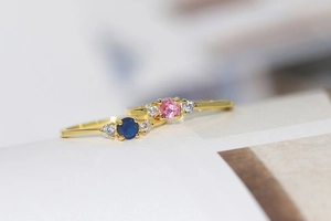 Macro shot of gold-plated rings with blue and pink zircon stones on textured paper