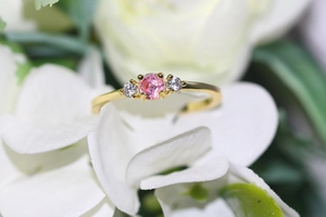 Detail of gold three-stone ring featuring a pink center stone and white side gems