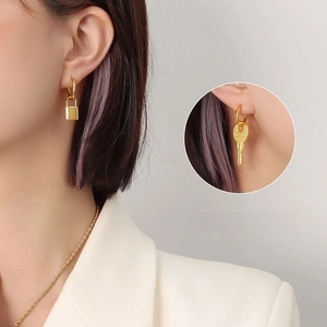 Detail view of gold asymmetrical earrings featuring lock and key charms on model
