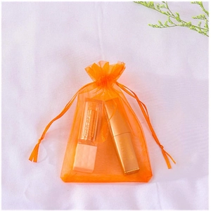 Detail of orange organza drawstring bag containing lipstick and cosmetics on white fabric