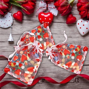 White organza gift bags with red hearts and colorful candies on a rustic wood background