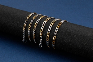 Polished gold and silver Cuban link bracelets displayed on a black textured cylinder