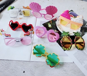 Flat lay of colorful party sunglasses with pineapple and shell designs on magazine