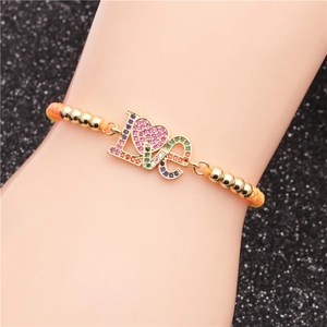 Makroaufnahme des orangefarbenen Armbands mit goldenem LOVE-Herzanhänger und Zirkon