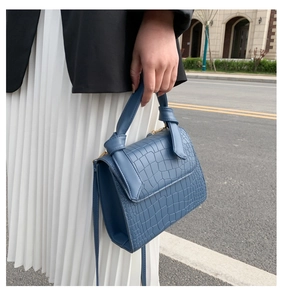 Detail view of blue crocodile pattern handbag featuring a unique knotted handle design
