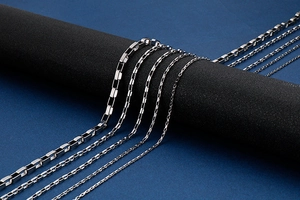Close-up of various silver chunky chain necklaces hanging on a black cylindrical stand