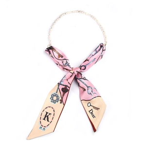 Détail du collier écharpe en soie rose avec perles et motif de clé vintage élégant