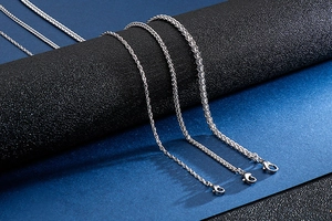 Close-up of stainless steel spiga wheat chains with lobster clasps on a black stand