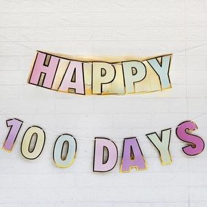 Pastellfarbene Happy 100 Days Girlande mit Goldrand an weißer Ziegelwand für Baby-Geburtstage