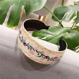 Detailed close-up of ethnic floral embroidery on a cream knotted headband with greenery