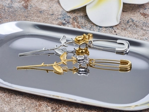 Detail of rose safety pin earrings in silver and gold metal finishes on a tray