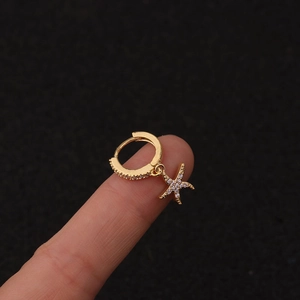 Macro detail of gold starfish earrings with clear zircons held against a black background