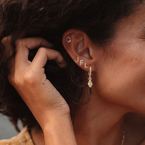 Detail of model wearing gold initial hoop earrings with sparkling cubic zirconia charms
