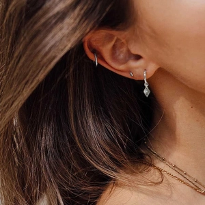 Close-up of S925 sterling silver evil eye hoop earrings and geometric studs on model