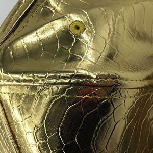 Détail de casquette en simili cuir crocodile doré avec œillet brodé et coutures